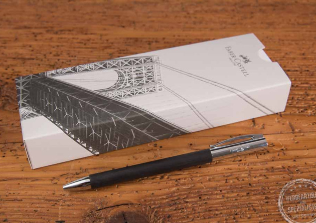 Faber-Castell AMBITION Kugelschreiber als Werbegeschenk vor Einzelverpackung liegend auf Holztisch.