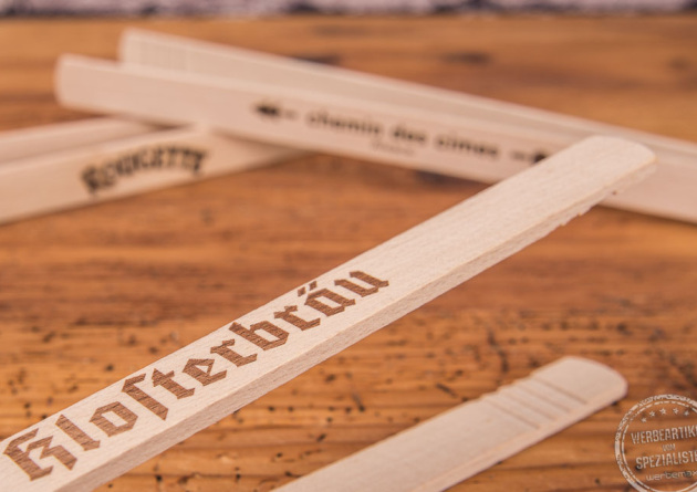 Grillzange aus Holz in Nahaufnahme mit einem individuellen Logo-Einbrand als Werbeartikel auf Holztischplatte.