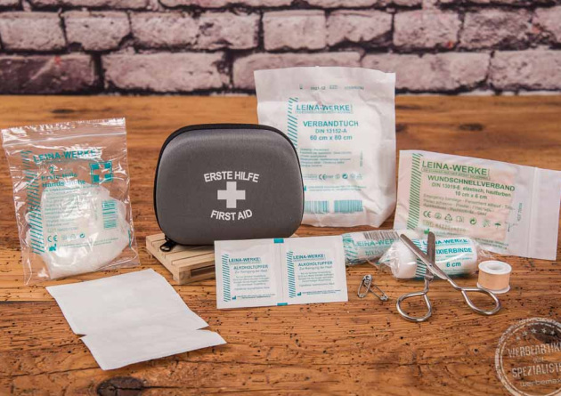 Graues Erste Hilfe Set als Werbegeschenk mit Schere, Mullbinden, Kleberolle, Pinzette und Handschuh universell f&uuml;r Erwachsene, Kinder oder Hunde einsetzbar.
