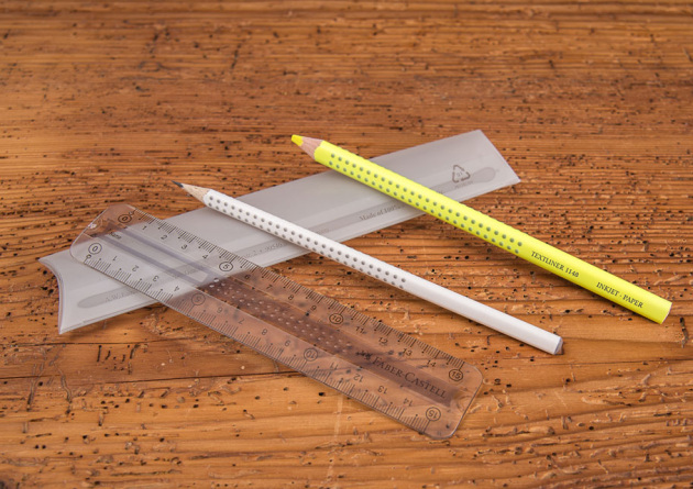 Faber Castell College Set Grip als Werbegeschenk mit Lineal, Bleistift und gelbem Stift zum Markieren aufgereiht &uuml;ber Verpackung liegend auf Holztisch.