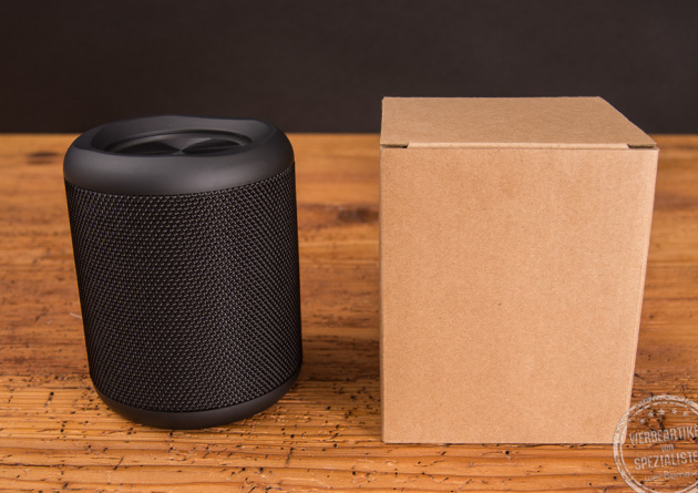 Bluetooth Lautsprecher in schwarz neben der Kartonverpackung aus Kraftpapier