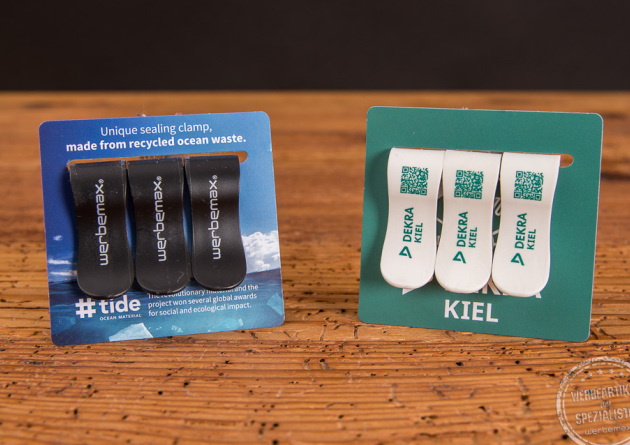 Bedruckte Beispiele der T&uuml;tenklammern Oceanclamps. Jeweils ein Dreierset-mit schwarzen sowie wei&szlig;en T&uuml;tenclips. Mit Logoaufdruck auf einen Kartonheader angeheftet.