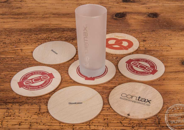Holzuntersetzer mit Logo bedruckt als Werbemittel mit Glas auf Holztisch.