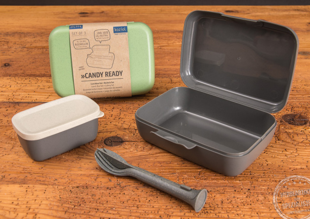 Ein geöffnetes graues koziol Candy Ready Lunchbox Set inklusive Besteck und kleiner auslaufsicheren Dose, sowie eine geschlossene grüne Candy-Ready Lunchbox. 