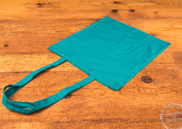 Cyanfarbene Messetasche mit langen Henkeln auf Holzuntergrund