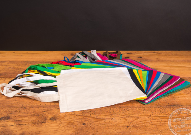 Messetasche in 22 Farben nebeneeinander aufgef&auml;chert liegend auf Holztisch