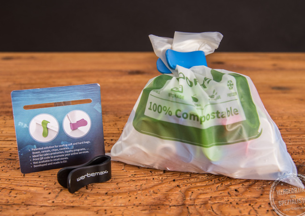 Recycelte T&uuml;tenclips aus Meeresplastik in schwarz mit wei&szlig;em werbemax Logodruck. Dahinter steht eine T&uuml;te, die mit den Oceanclamps verschlhossen wurde. 