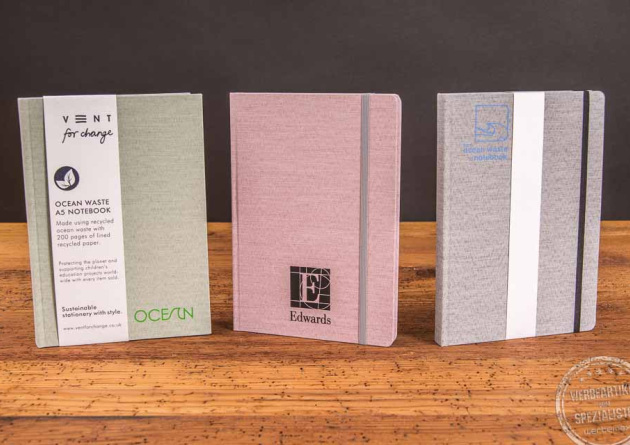 Drei stehende Ocean Book Notizbücher in den Farben grün, rot und grau als Werbeartikel. 