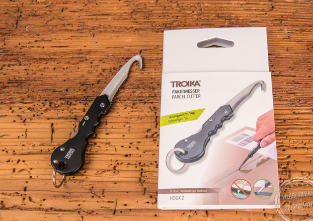 Paketmesser Troika Hook2 geöffnet liegend neben der Verpackung als Werbegeschenk.