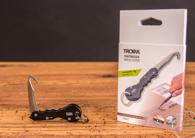 Troika Paketmesser Hook2 geöffnet liegend vor der Verpackung. 