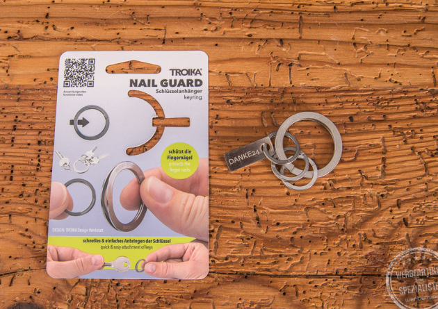Troika Schlüsselanhänger Nail Guard liegend neben der Verpackung als Werbeartikel. 