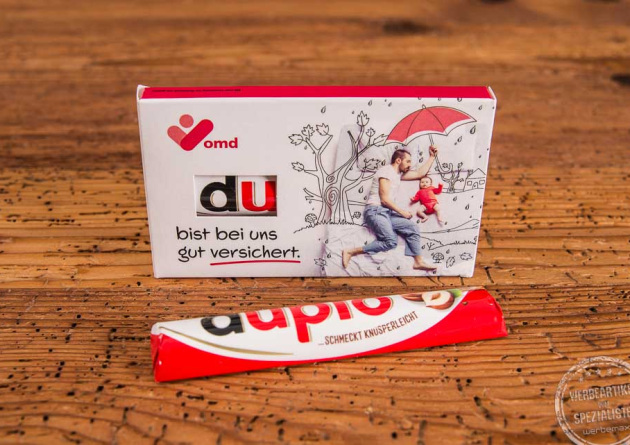Duplo Schokoriegel im individuell bedruckten Werbeschuber mit der Aufschrift „Du bist bei uns gut versichert“ und goldenem Herzdesign – ideal als emotionales Give-away für Mitarbeiter und Kunden.