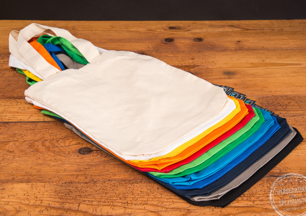 Hochwertige Messetasche mit Bodenfalten aufgef&auml;chert um die gro&szlig;e Farbvielfalt besser zu sehen auf Holztisch &uuml;bereinander liegend.