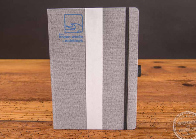 Stehendes graues Ocean Waste Notizbuch mit Logo als Werbeartikel. 