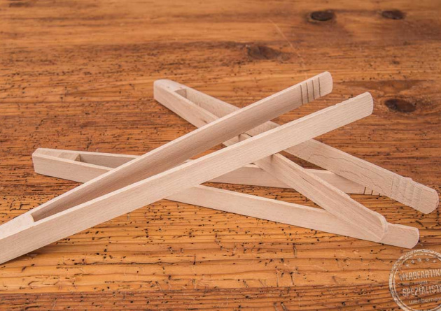 Drei Grillzangen aus Holz, aufeinandergelegt, mit individuellem Logo durch einen Einbrand (Logobranding) auf Holztischplatte.