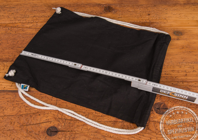 schwarzer Matchrucksack aus Fairtrade Baumwolle mit naturfarbenen Baumwollkordeln. Ein Meterstab zeigt die genaue Höhe des Turnbeutels. 
