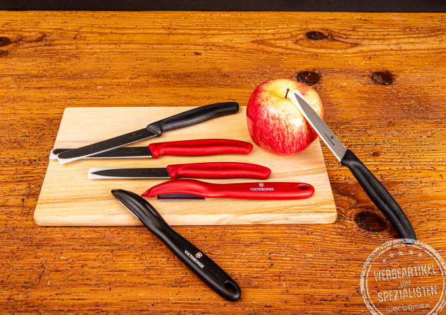 Victorinox Gemüsemesser mit schwarzem und rotem Griff inkl. Sparschäler liegend auf Frühstücksbrett.