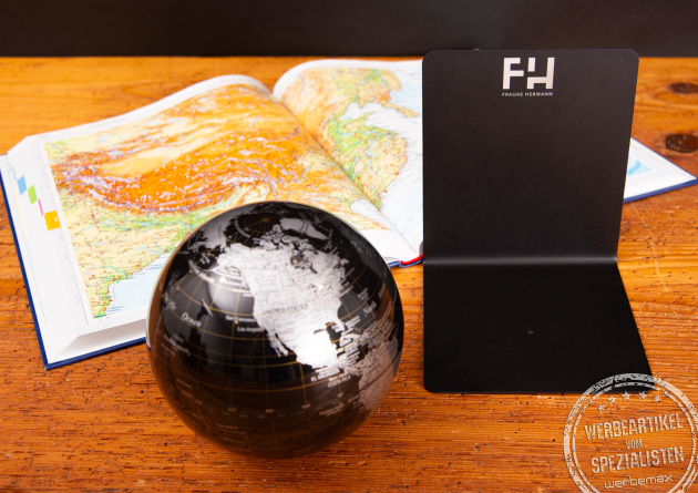 Troika Globus und mattschwarze Buchst&uuml;tze mit Logogravur neben aufgeschlagenem Diercke Atlas auf Holztisch.