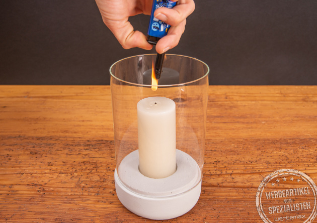 Eine Windlicht, dessen Kerze mit einem Werbe-Stabfeuerzeug angez&uuml;ndet wird.