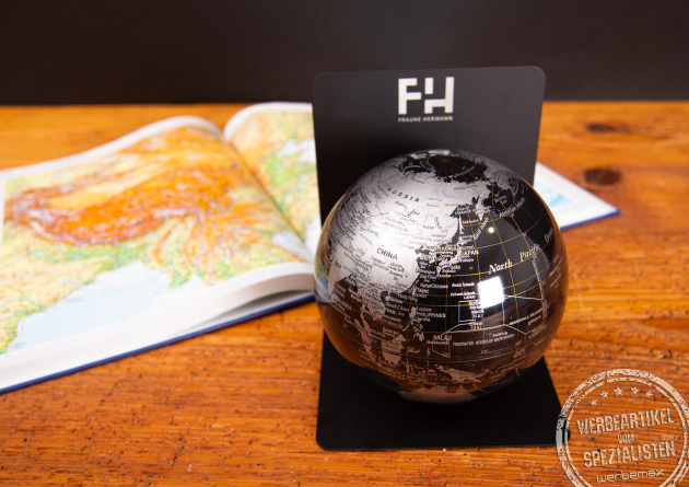 Metallschwarzer, magnetischer Troika Globus auf Buchst&uuml;tze neben aufgeschlagenem Diercke Atlas auf Holztisch.