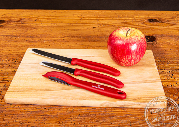 Zwei Victorinox Gemüsemesser und ein Schäler mit rotem Griff liegend auf einem Frühstücksbrett.
