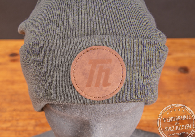 Graue Beanie mit runden PU-Patch als Werbeartikel.
