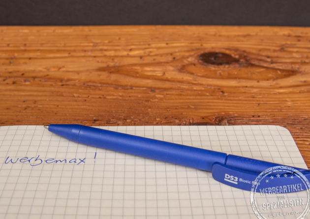 Ein blauer Werbekugelschreiber mit Logo liegend auf einem karierten Blatt Papier.