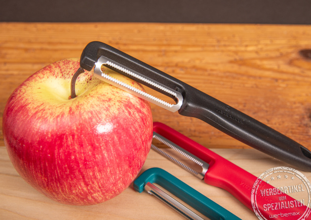 Victorinox Sparschäler Iota in drei Farben mit Apfel auf Holzunterlage.