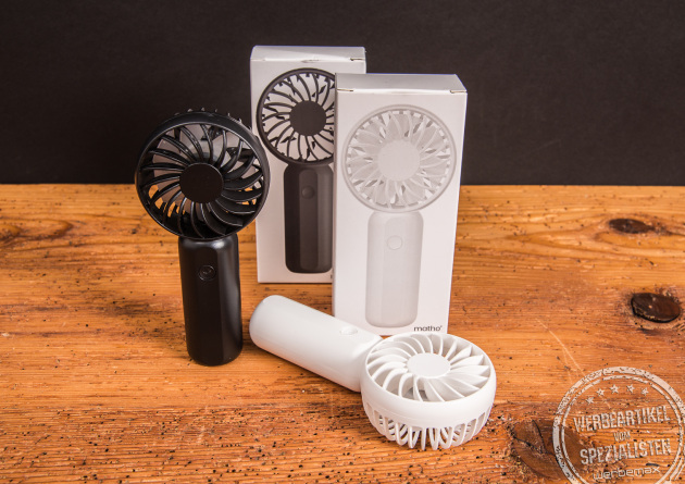 Handventilator Breezy als Werbeartikel in Schwarz und Weiß mit Logo-Fläche, jeweils mit Einzelverpackung – modernes Sommer-Promotion-Geschenk auf Holzplatte.