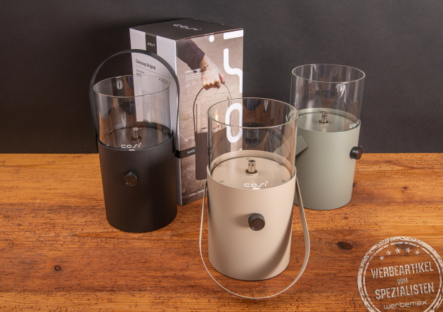 Cosiscoop Original Gaslaternen in Schwarz, Beige und Olivgrün mit Verpackung auf Holztisch – hochwertiges Outdoor-Licht als Werbegeschenk mit Logo