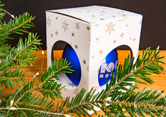 Blaue Weihnachtskugel mit Logo in weißer Geschenkbox mit goldenen Sternen dekoriert mit Tannenzweigen als Merchandise Geschenk für Sport- und Musik-Fans.