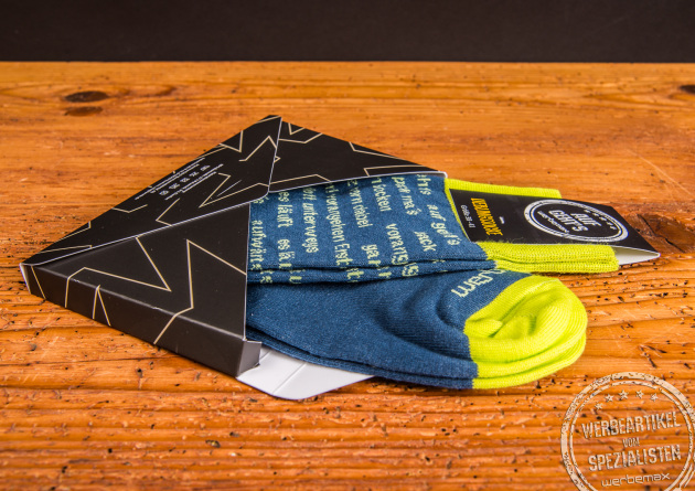 Bequeme Eigendesign-Socken mit Ihrem Logo in der versandf&auml;higen Mailingbox auf Holztisch.
