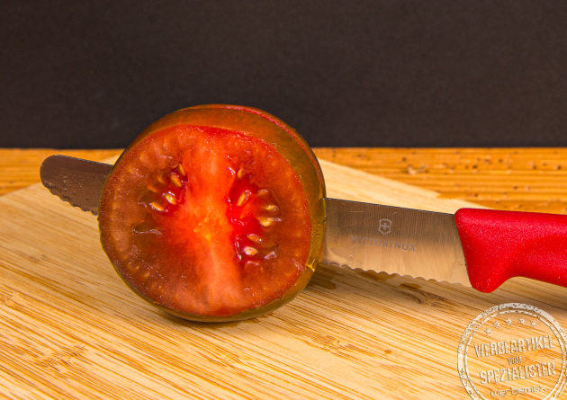Victorinox Tomatenmesser mit rotem Griff schneidet eine frische Tomate &ndash; scharfes K&uuml;chenmesser mit individueller Logogravur als Werbeartikel.