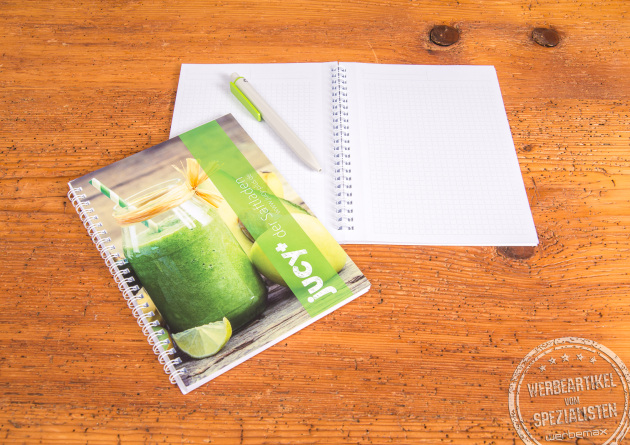 Günstiges A5 Notizbuch mit Spiralbindung und individualisiertem Titelblatt, ideal als Werbeartikel oder Kundengeschenk. Abgebildet auf Holztisch mit passendem Stift und aufgeschlagenen Seiten.