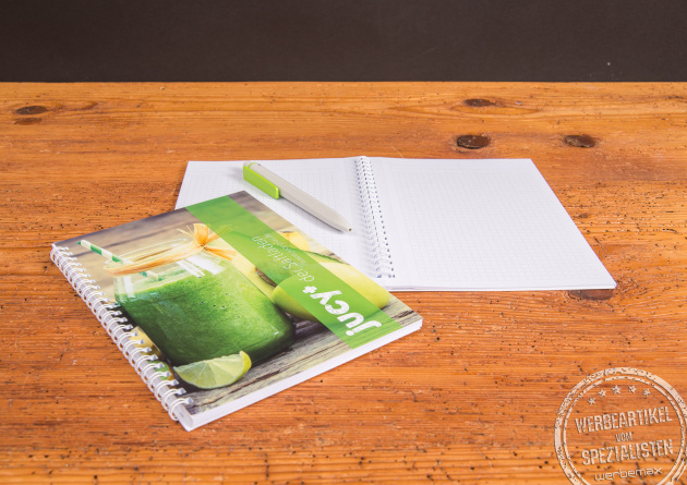 A5 Notizbuch mit Spiralbindung und individuell bedrucktem Cover im modernen Design, aufgeklappt auf Holztisch mit passendem Stift – ideales Meeting Book als günstiger Werbeartikel für Notizen, Seminare und Kundengespräche.