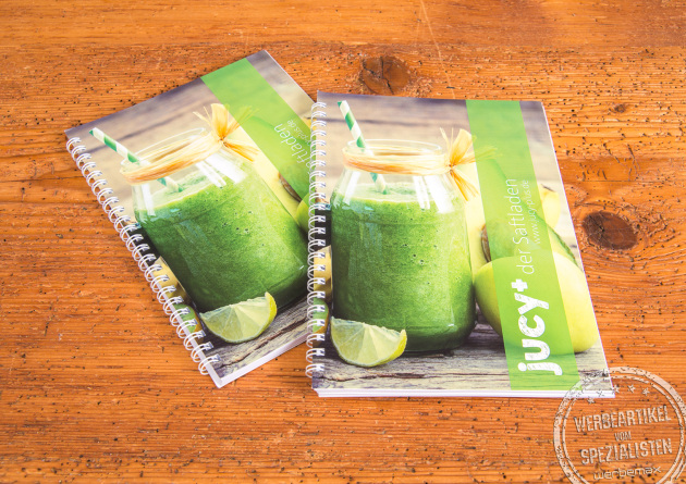 Zwei A5-Notizb&uuml;cher mit Spiralbindung und individuell bedrucktem Titelblatt im frischen Design mit gr&uuml;nem Smoothie-Motiv, abgebildet auf Holztisch &ndash; ideale, personalisierbare Werbeartikel f&uuml;r Meetings, Schulungen und Events.