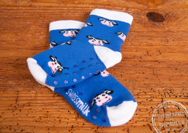 Blaue Babysocken mit Anti-Rutsch-Noppen und Einwebungen eines Kuhmotives. Die Babysocken liegen auf einem Holztisch.