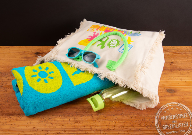 Strandtasche Promotion Fairtrade &ndash; gef&uuml;llte Canvas-Badetasche mit Handtuch, Sonnenbrille und neonfarbenen Kordeln auf Holztisch