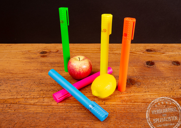 Jumbo Textmarker im XL-Format als Riechstifte in leuchtenden Farben auf Holztisch, dekoriert mit Apfel und Zitrone &ndash; kreative Werbeartikel und auff&auml;llige Giveaway-Idee f&uuml;r Messen und Promotion-Aktionen.