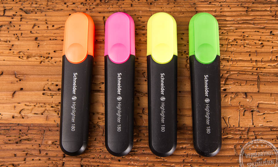 Die vier Standardfarben der Textmarker nebeneinander. Orange, Pink, Gelb und Grün liegen auf einem Holztisch nebeneinander