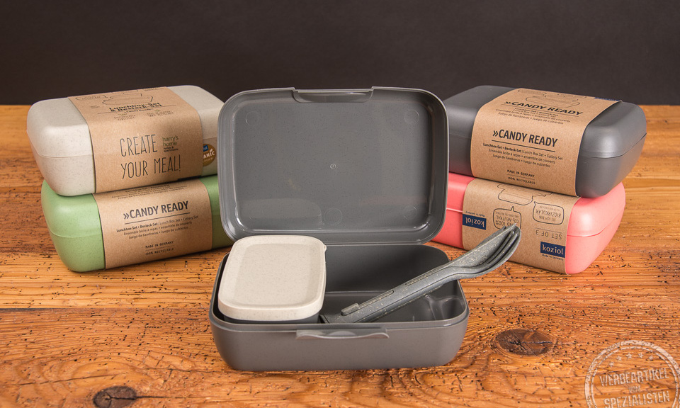 Mehrere koziol Brotdosen in unterschiedlichen Farben mit Werbebanderole und Besteck-Set.