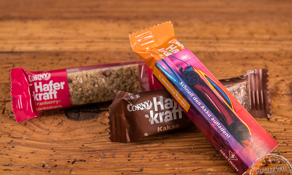 Corny Haferkraft Riegel als Give-away auf Messen im individuell bedruckten Kartonschuber auf Holztisch.