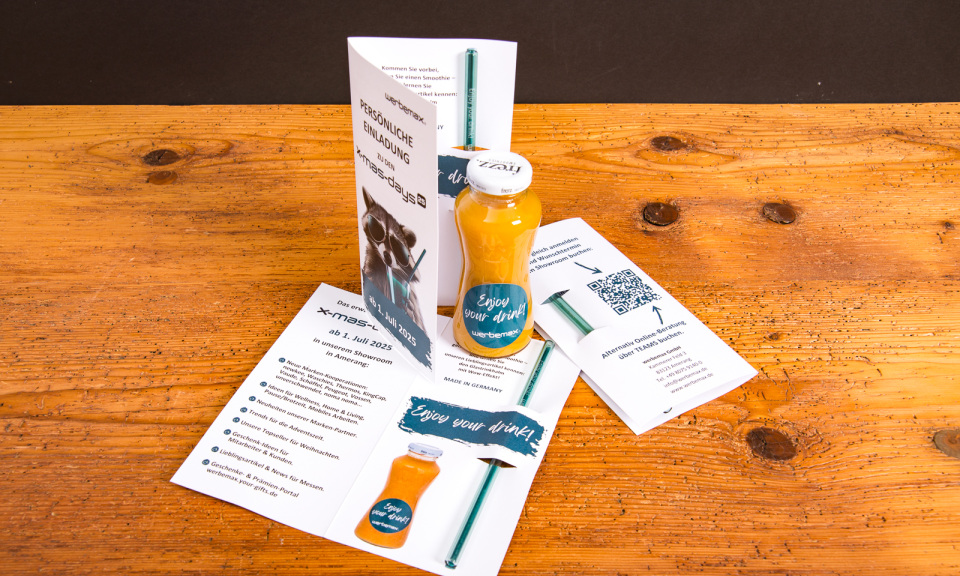Einladung zu den werbemax xmasdays 2025 mit Flyer, Glasstrohhalm, Smoothieflasche mit „Enjoy your drink“-Aufdruck und QR-Code – kreative Werbeartikel-Präsentation auf Holztisch.