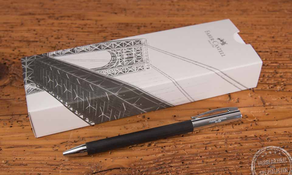 Faber-Castell AMBITION Kugelschreiber als Werbegeschenk vor Einzelverpackung liegend auf Holztisch.