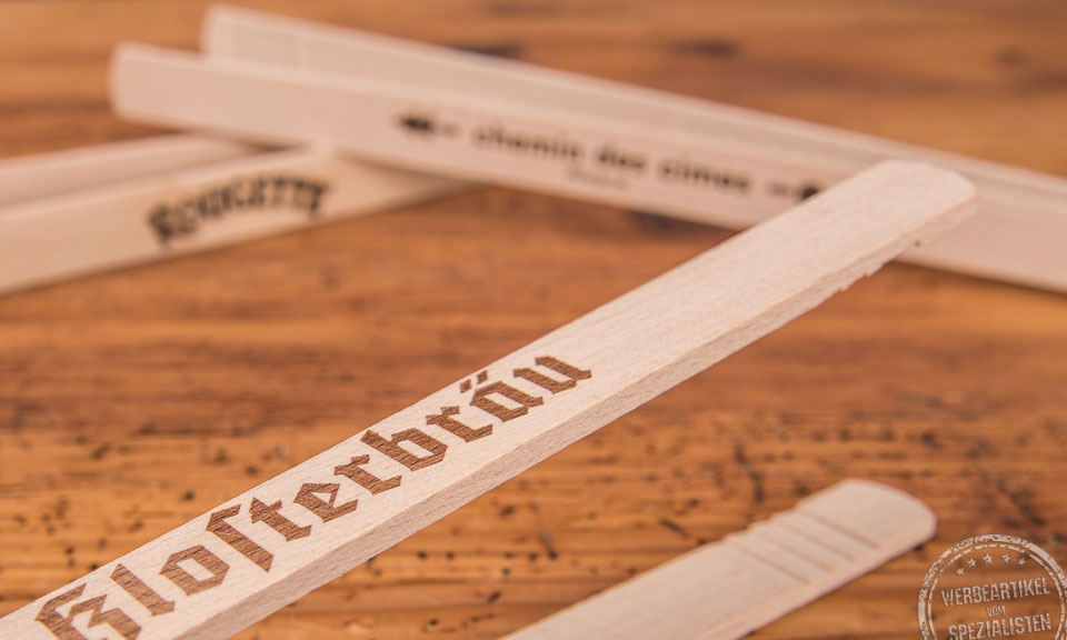 Grillzange aus Holz in Nahaufnahme mit einem individuellen Logo-Einbrand als Werbeartikel auf Holztischplatte.