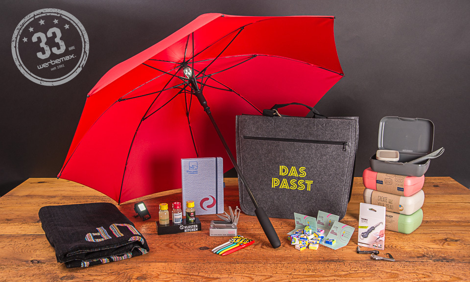 Verschiedene Jubil&auml;ums-Werbeartikel wie ein roter Regenschirm, ein Handtuch, Ahoj Brause, Koziol-Mehrwegartikel als Werbegeschenke. 
