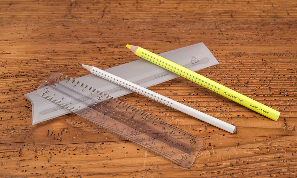 Faber Castell College Set Grip als Werbegeschenk mit Lineal, Bleistift und gelbem Stift zum Markieren aufgereiht &uuml;ber Verpackung liegend auf Holztisch.