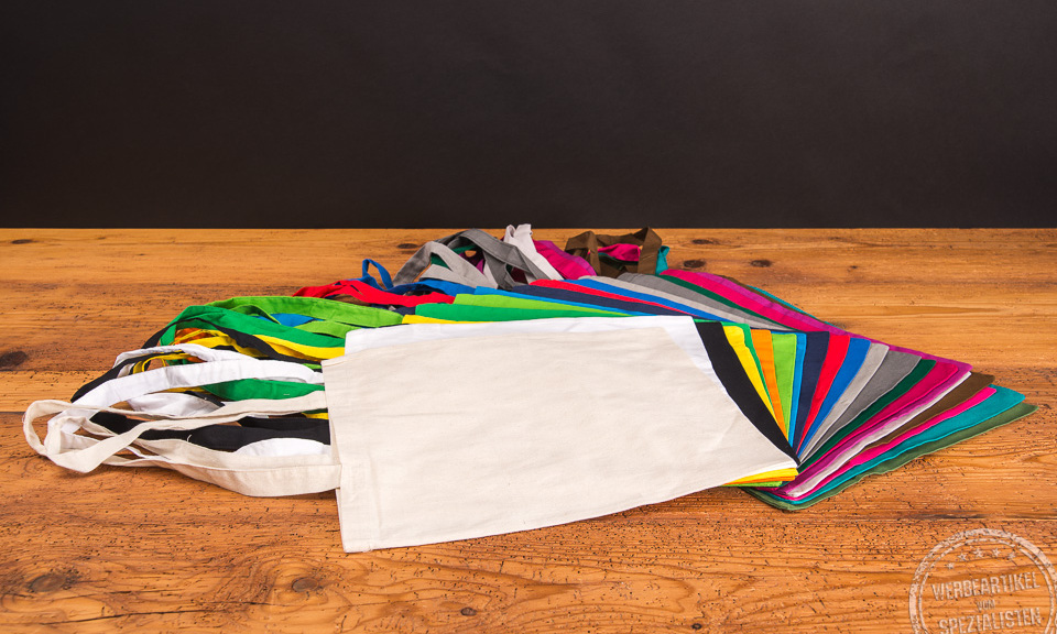 Messetasche in 22 Farben nebeneeinander aufgef&auml;chert liegend auf Holztisch