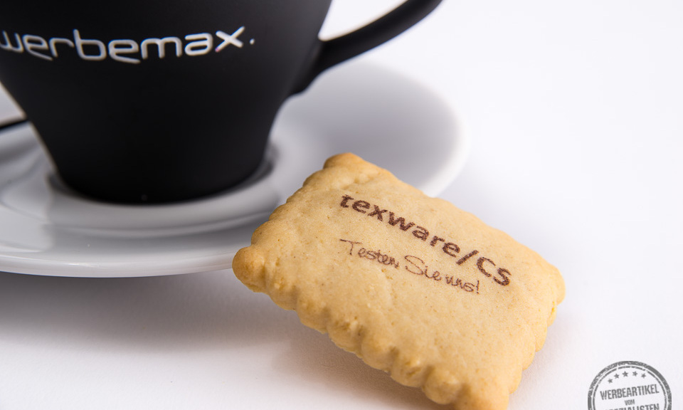 Butterkeks mit einem Logo bedruckt neben einer Tasse Cappuccino als Werbegeschenk.