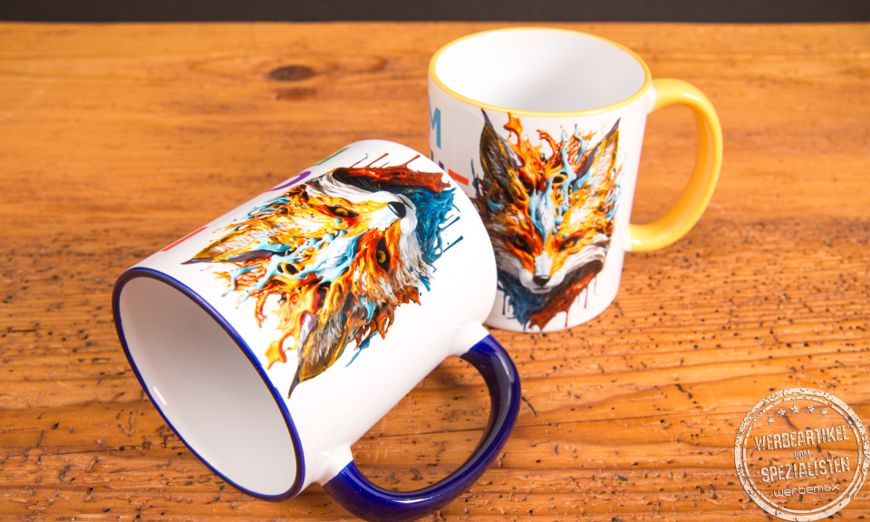 Zwei individuell bedruckte Keramik-Tassen mit farbigem Henkel und kreativem Fuchs-Motiv &ndash; hochwertige Werbeartikel Tassen von Werbemax auf Holztisch.